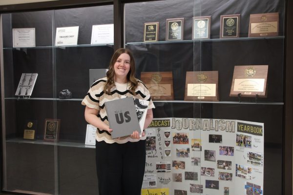Journalism teacher Kelly Delgado stands in front of the journalism trophy case with the yearbooks she's worked on while at RHS. 